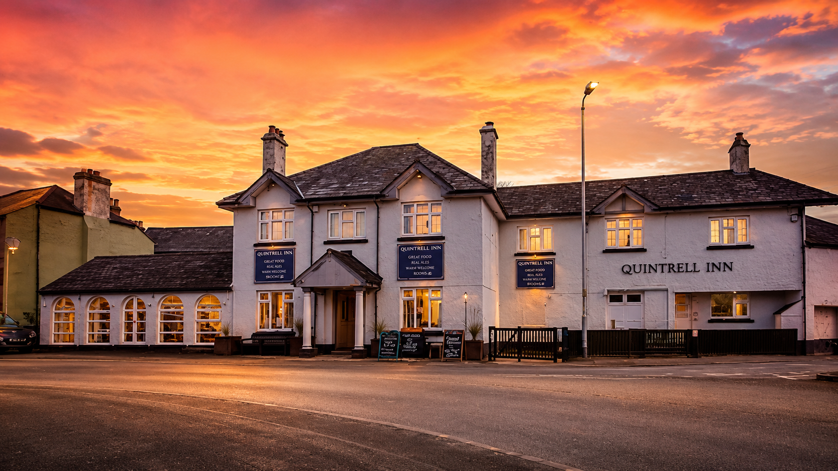 The Quintrell Inn, a traditional white-fronted Cornish pub near Newquay, lit warmly against a vivid sunset sky